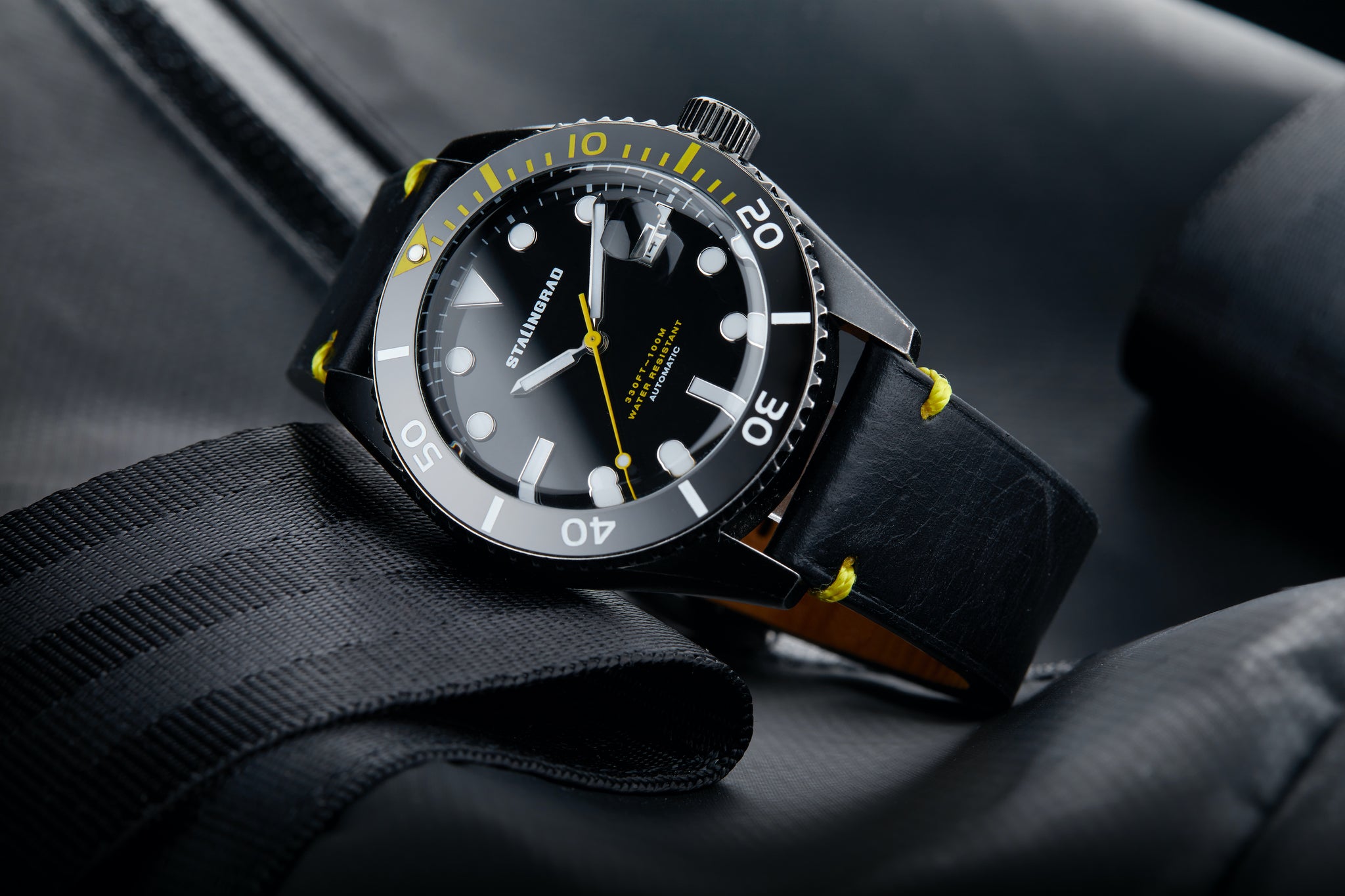 Stalingrad Volga defender automatic watch with a black case and black dial with yellow accents in a black leather strap, diagonal view of watch on a dark background
